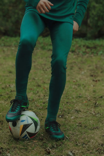 Person in green merino outfit attire with a soccer ball on grass