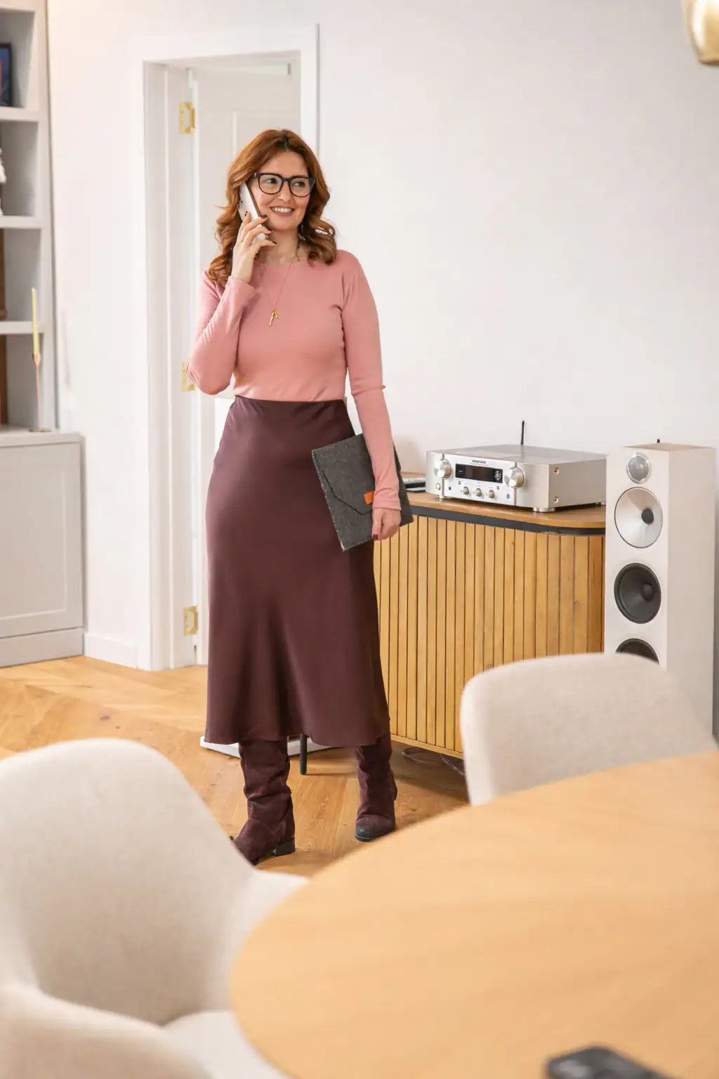 Woman in a pink top and brown skirt standing in a modern living room.