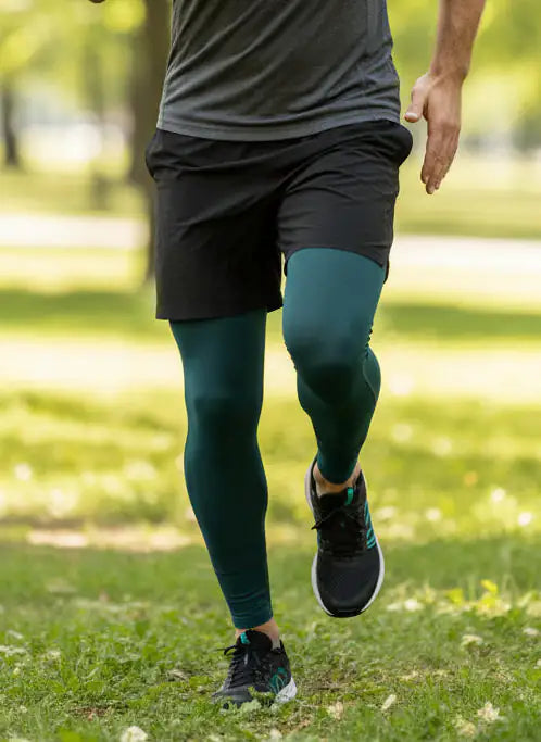 Person wearing dark green merino leggings and black athletic shoes walking on grass