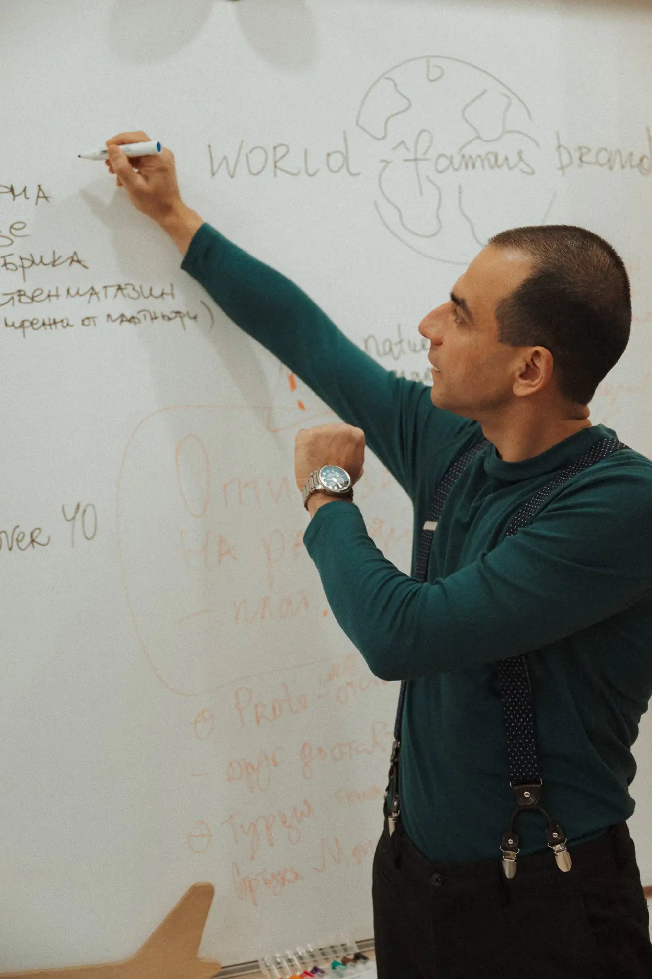 Man writing on a whiteboard with text and diagrams wearing a green merino top