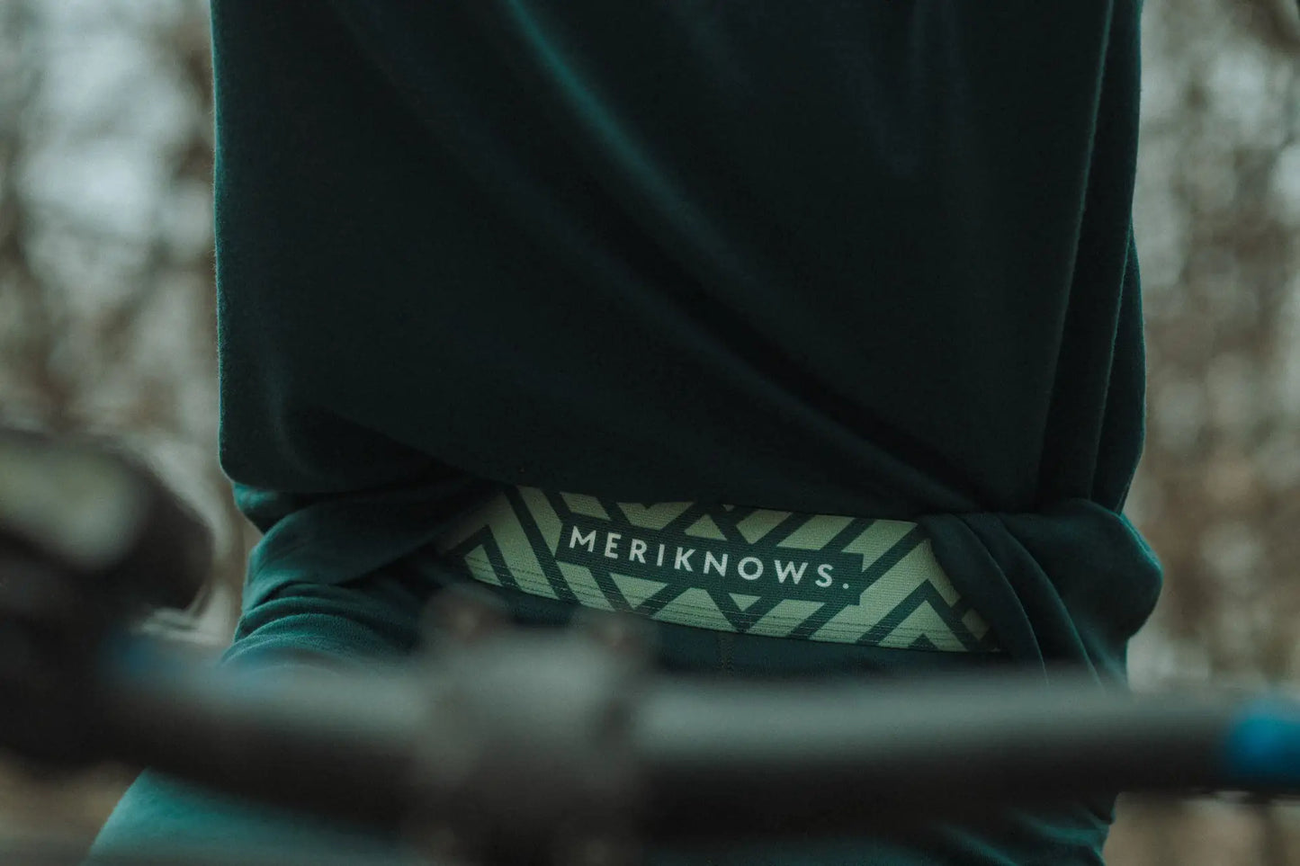 Person wearing a green merino leggings  with 'MERIKNOWS' logo on a blurred background