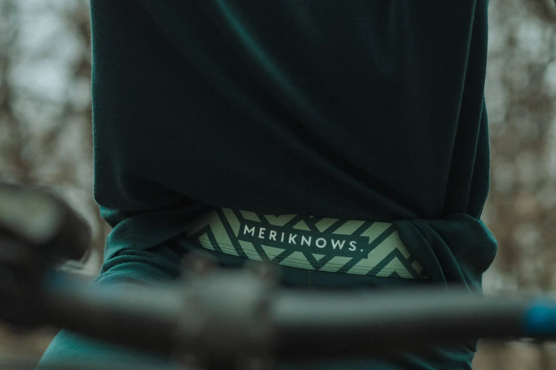 Person wearing a green merino leggings  with 'MERIKNOWS' logo on a blurred background