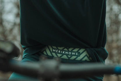 Person wearing a green merino leggings  with 'MERIKNOWS' logo on a blurred background