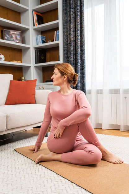 Woman in pink outfit practicing yoga in a merino wool set on a mat in a living room.