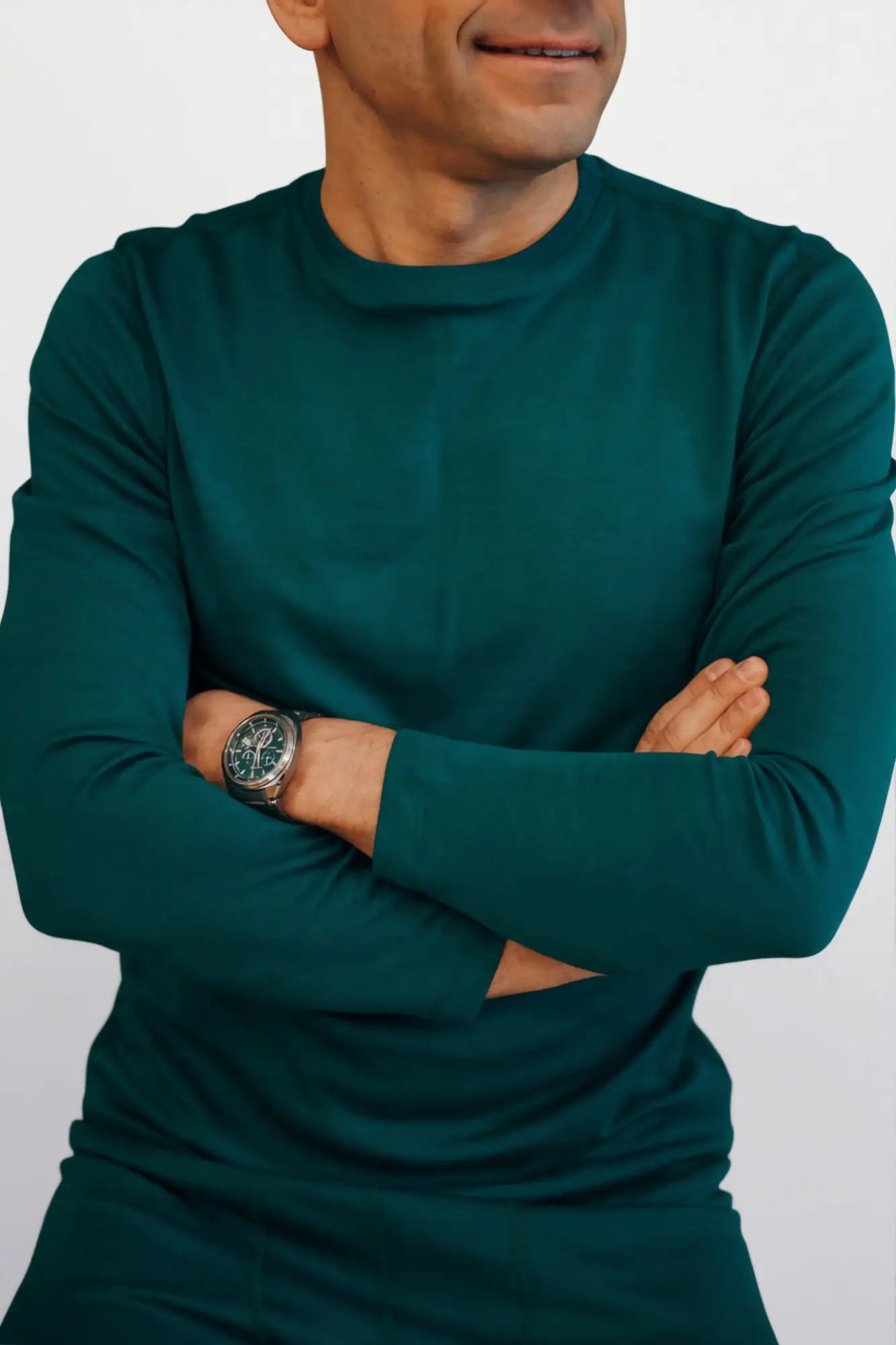 Man wearing a teal long-sleeve merino wool top with arms crossed against a white background
