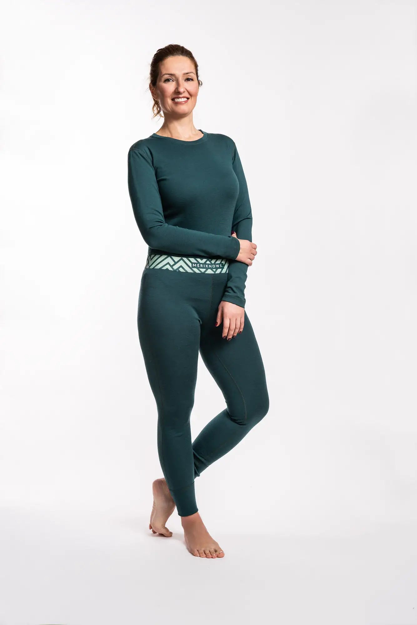 Woman wearing a green long-sleeve fine merino top and leggings with a white background