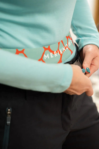 Person wearing a light blue long-sleeve merino shirt with red branding, holding a black object.