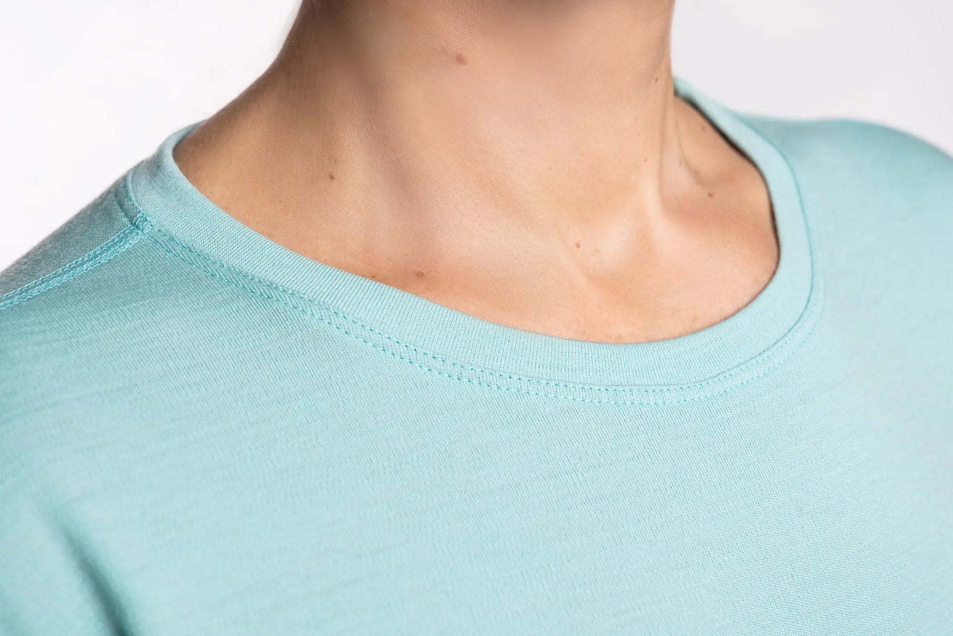 Close-up of a person wearing a light blue merino shirt with a plain background